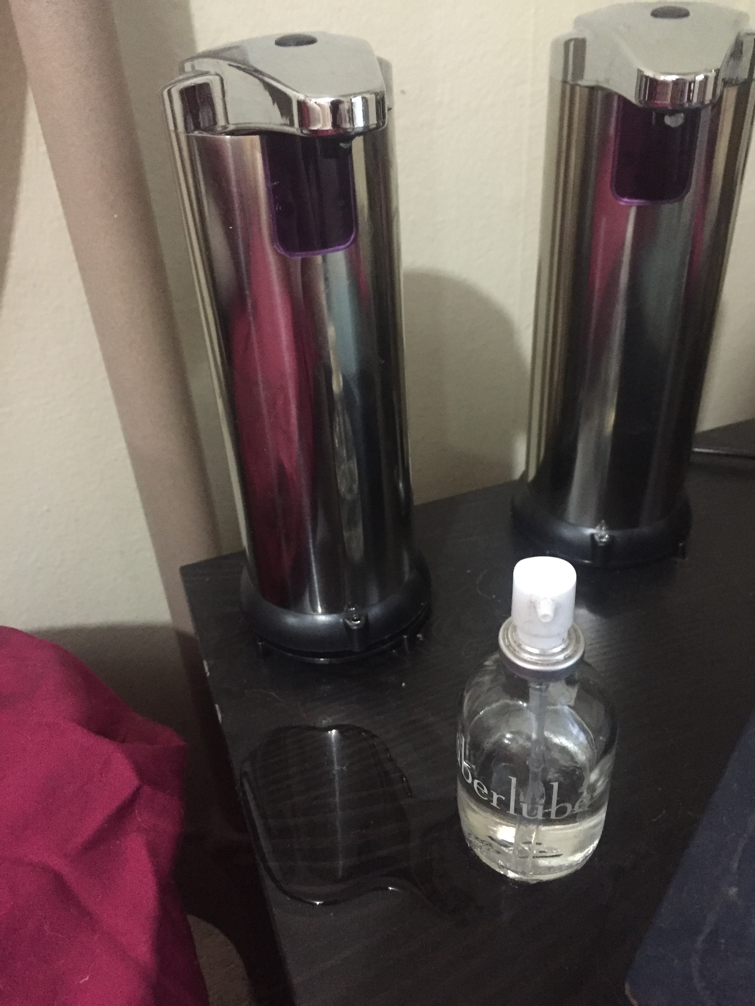 two silver automatic soap dispensers and a small glass pump bottle of uberlube