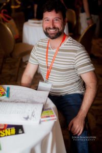 Bearded 2016 Sex Geek attendee looks up from a coloring book to smile for the camera