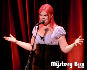 JoEllen in a purple and black dress speaking on stage