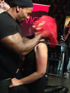 Muscular man in a black hat and shirt holding JoEllen's head on a spanking bench at a Pleasure Chest Party