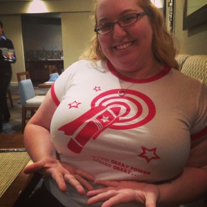 A Blonde woman wearing a white t-shirt with red rings around the neck and sleeves and a red vibrator design