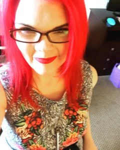 JoEllen taking a selfie with bright red hair, dark glasses, and a black and white dress with flowers on it.