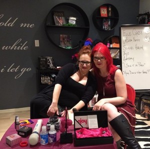 Two women, both redheads, pose on a small stage in a sex shop
